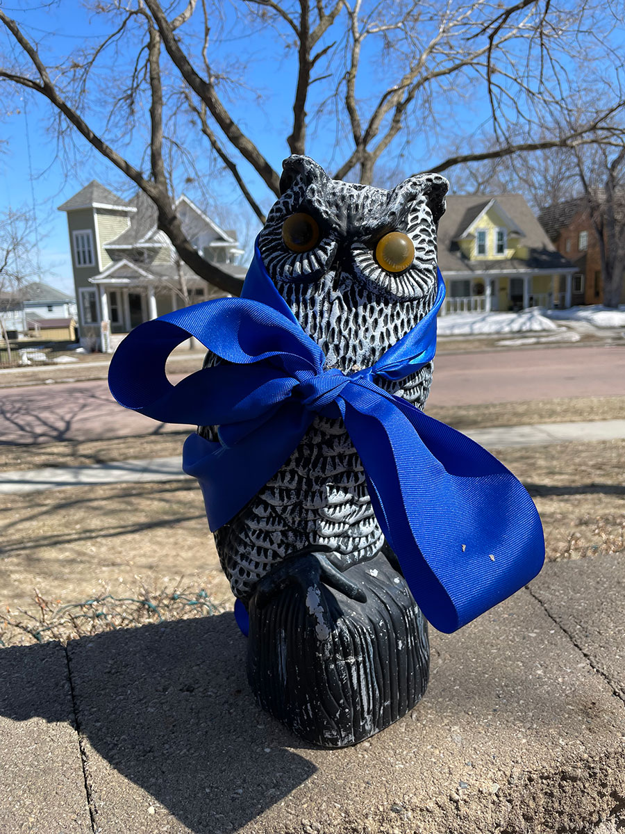 Blue ribbon tied around an owl statue.