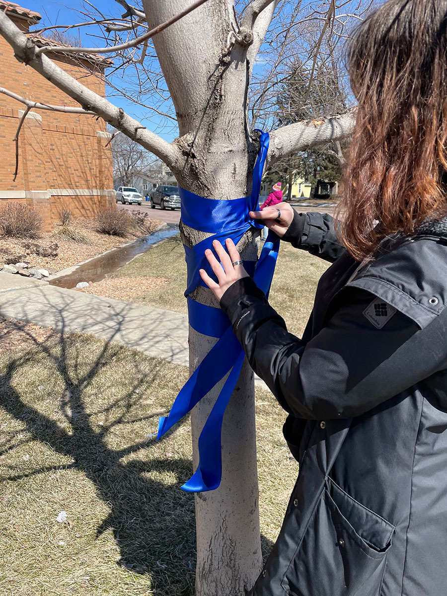 Girl tying Blue Ribbon around a tree.